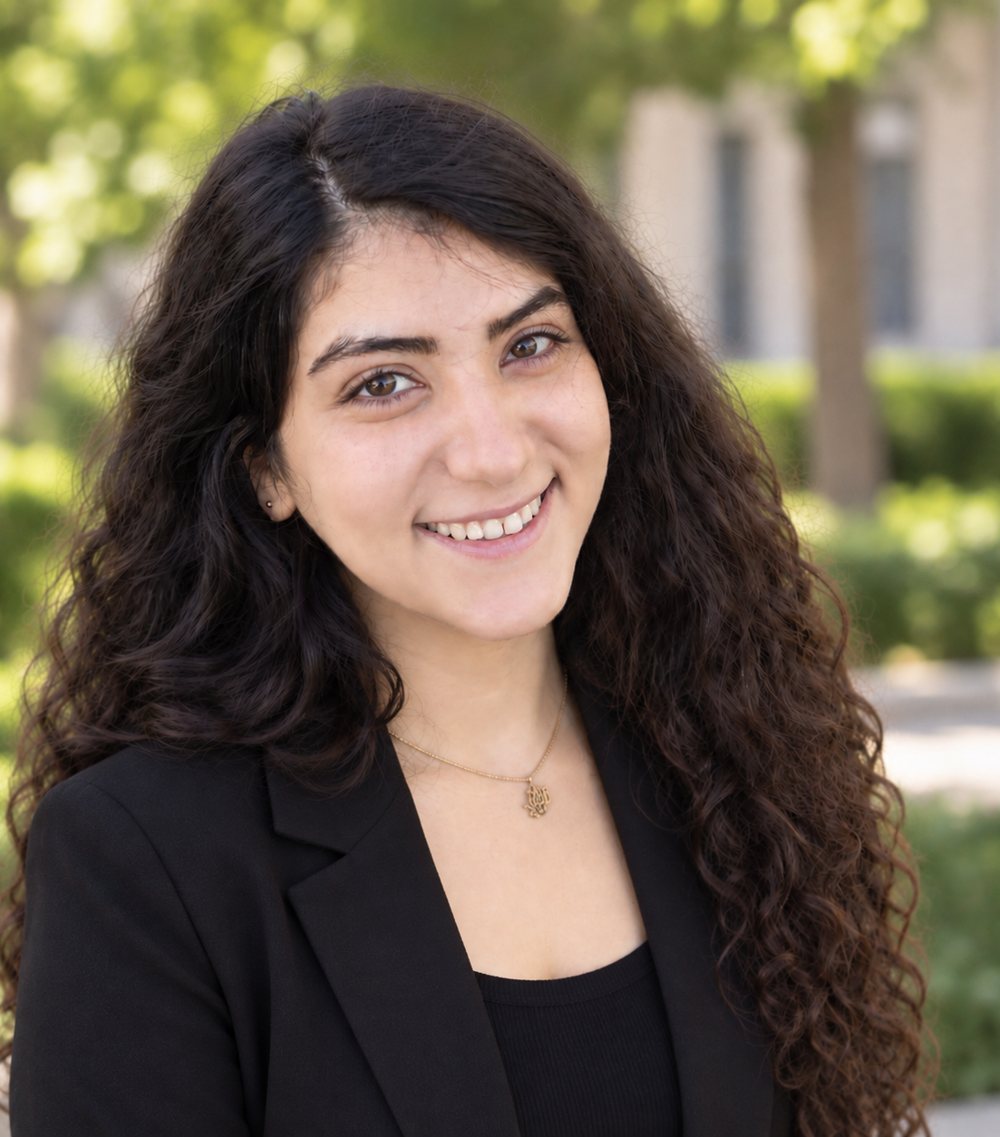 Portrait of Niloofar Banaei smiling, with long curly dark hair and a black blazer